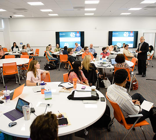 Clemson faculty and staff sit at round tables in the Watt Innovation Center during a training session.