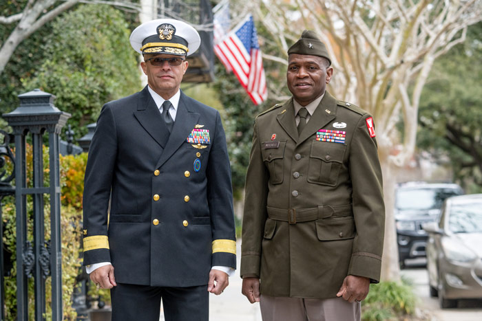A man wearing a navy blue U.S. Navy dress uniform stands next to a man wearing an olive green U.S. Army dress uniform.