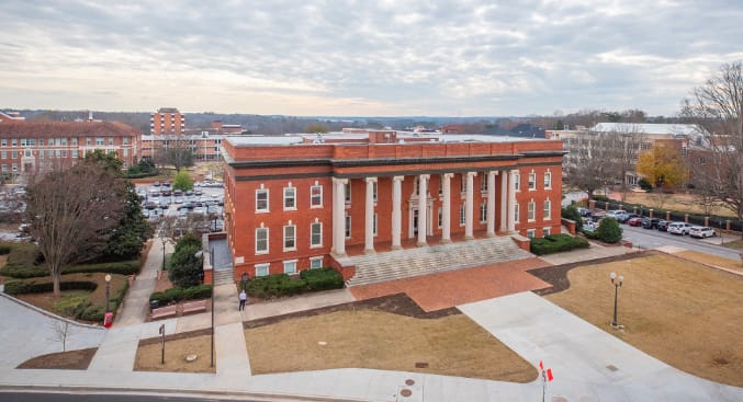 Sikes Hall, a traditional red brick building, sits in front of a variety of academic buildings on Clemson's campus.