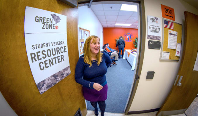A female employee smiles, opening the door to the student veteran resource center.