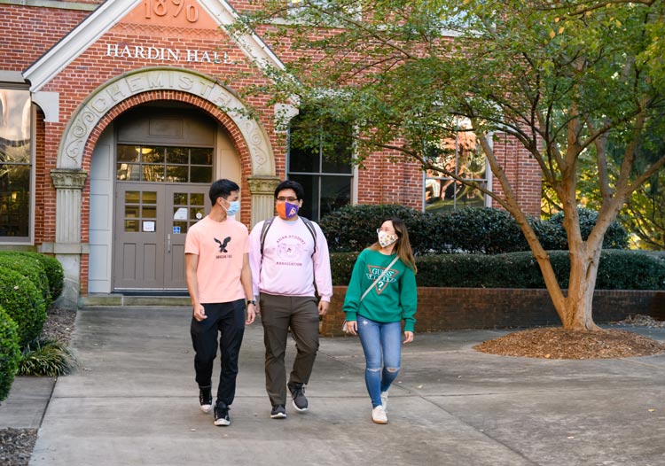 Three masked students exit a brick academic building together.