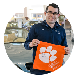 Student Ryan Sweeney holds an orange Tiger Rag emblazoned with a white Clemson Paw while standing in a showroom at BMW. 