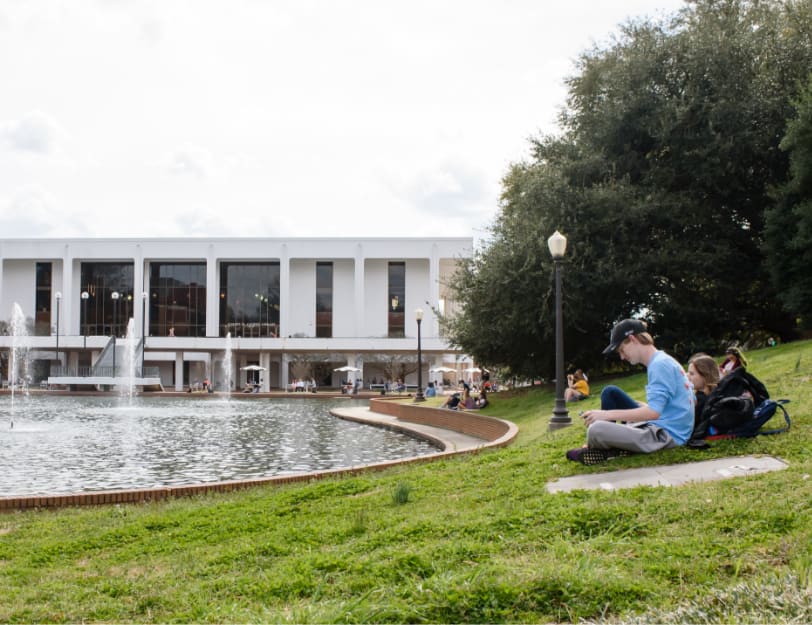 Clemson students study while sitting in the grass beside the reflection pond and Cooper Library.