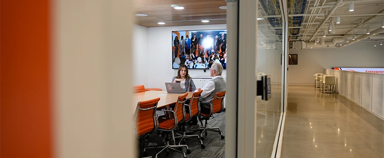 a female student speaks with a staff mentor from the exterior of an office with glass walls