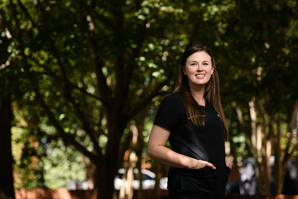 A woman wearing black medical scrubs poses outside on the Clemson University campus. 
