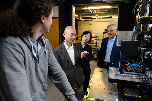 Two male researchers, one female researcher and a male student gather around a device in Clemson University’s Advanced Material Research Laboratory.
