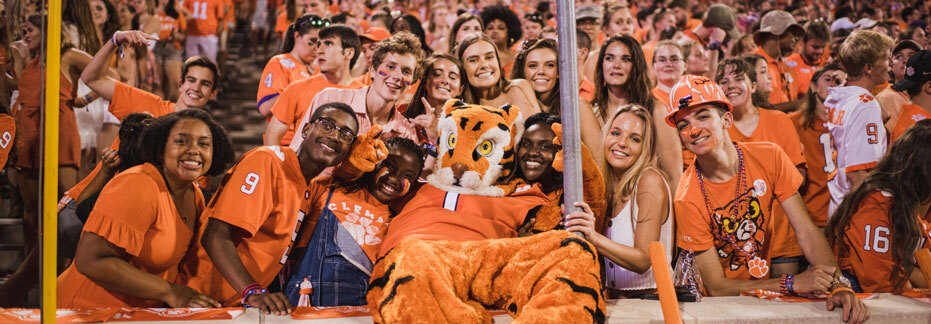 The Tiger mascot reclines and poses with orange-clad students on the front row of Death Valley during a night football game. 