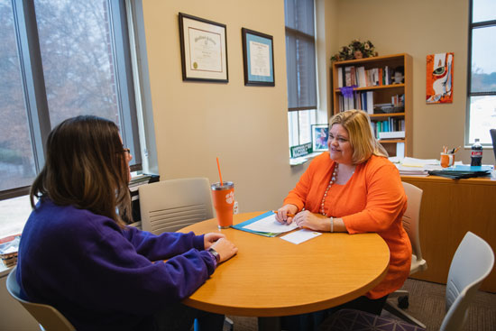 An female advisor and student sit around a table in her office having a friendly conversation
