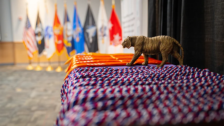 Red, white and blue graduation cords with orange stoles sit on a table along with a small tiger statue.