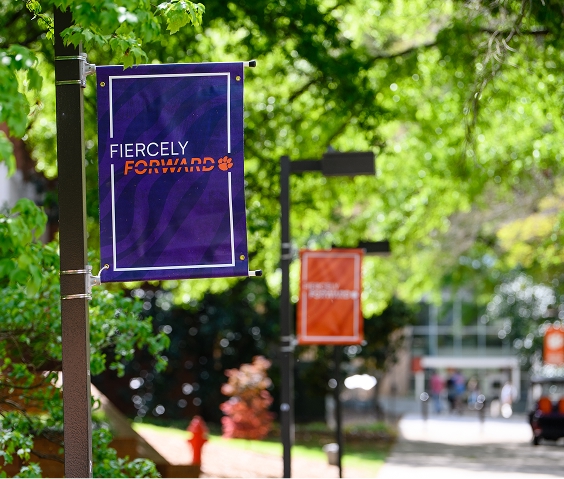 A purple banner that says Fiercely Forward is hung up on Clemson's campus.