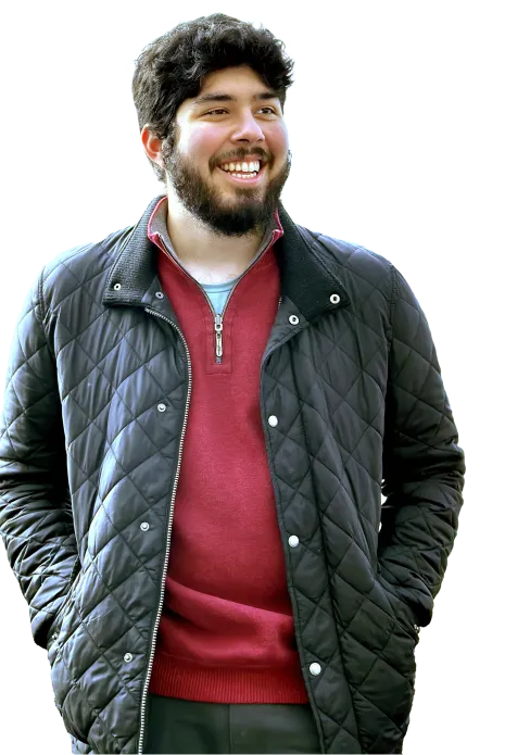 A male student wearing a red quarter-zip sweater and black winter jacket smiles and looks off camera.