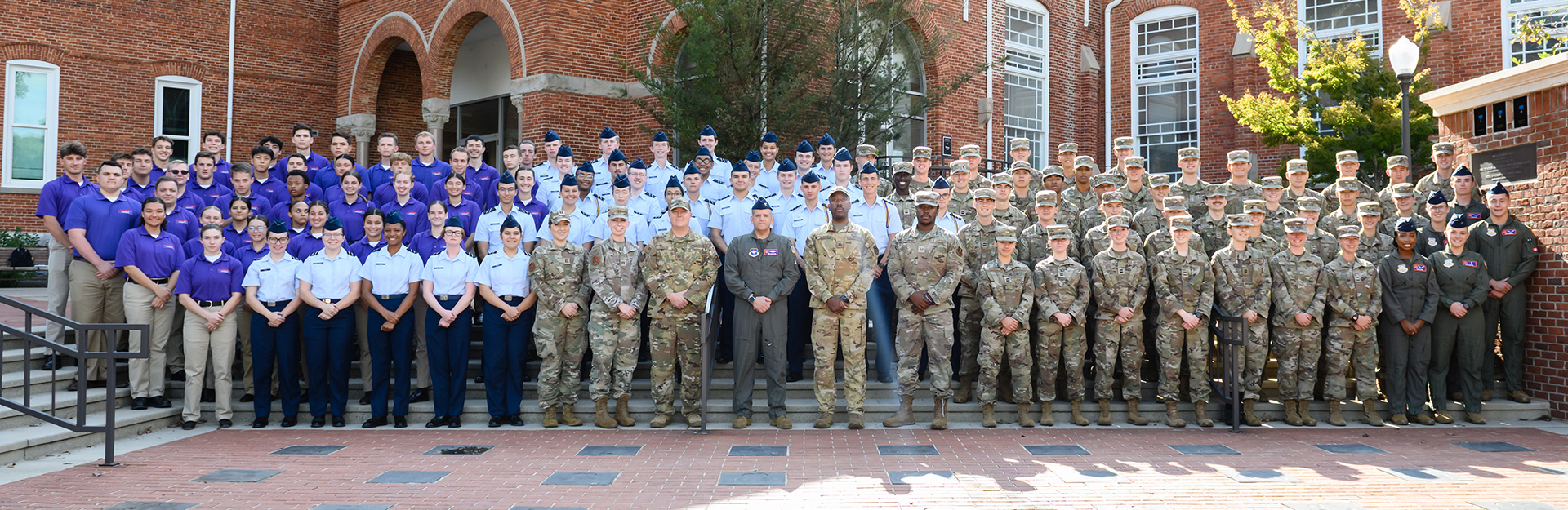 Group photo of male and female students in Air Force camouflage and uniforms standing in front of Tillman Hall.