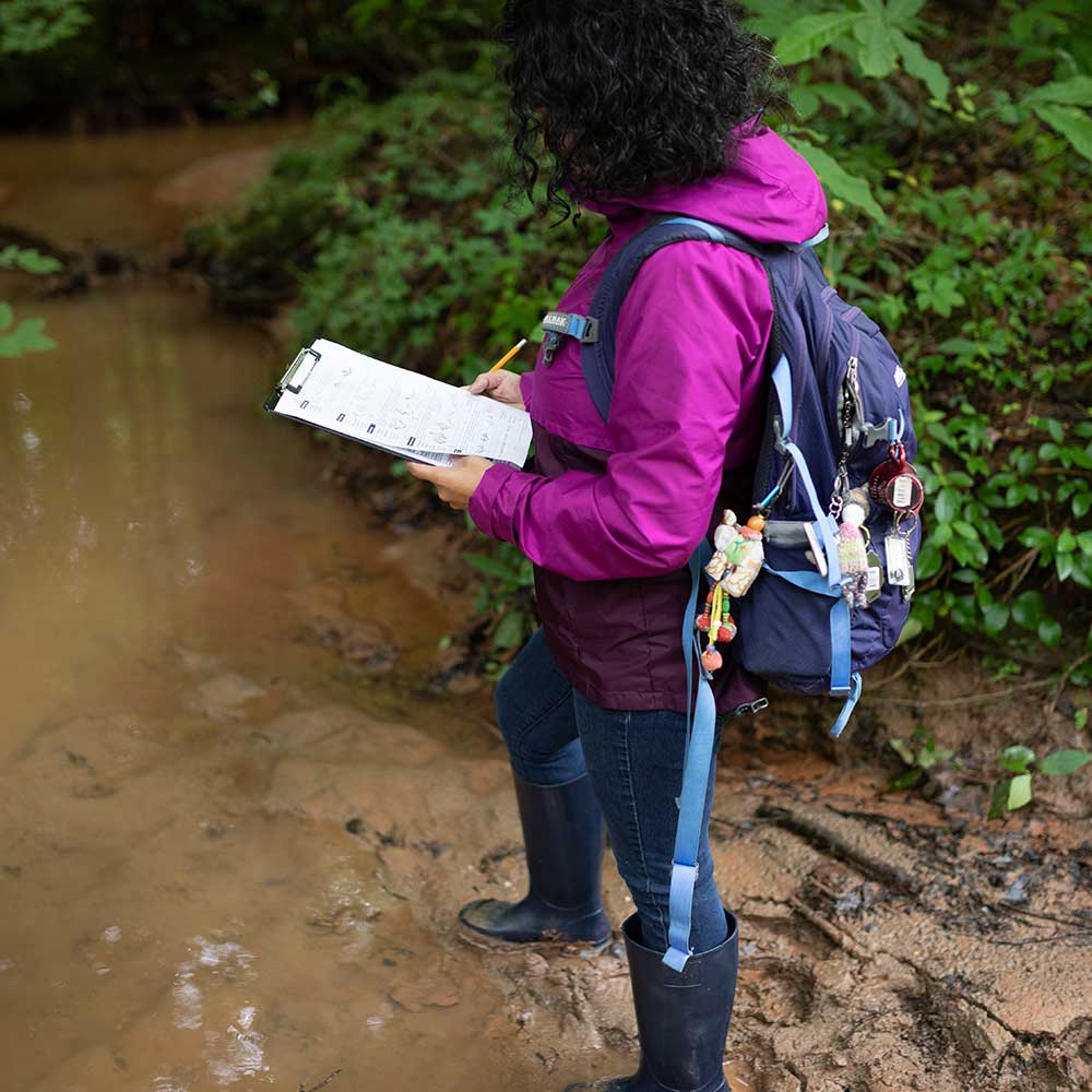 woman in creek recording data on a clipboard