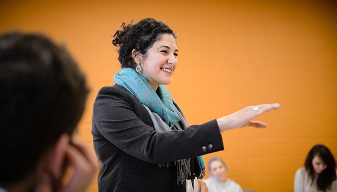 Professor Angela Naimou smiles and gestures while speaking to a class.