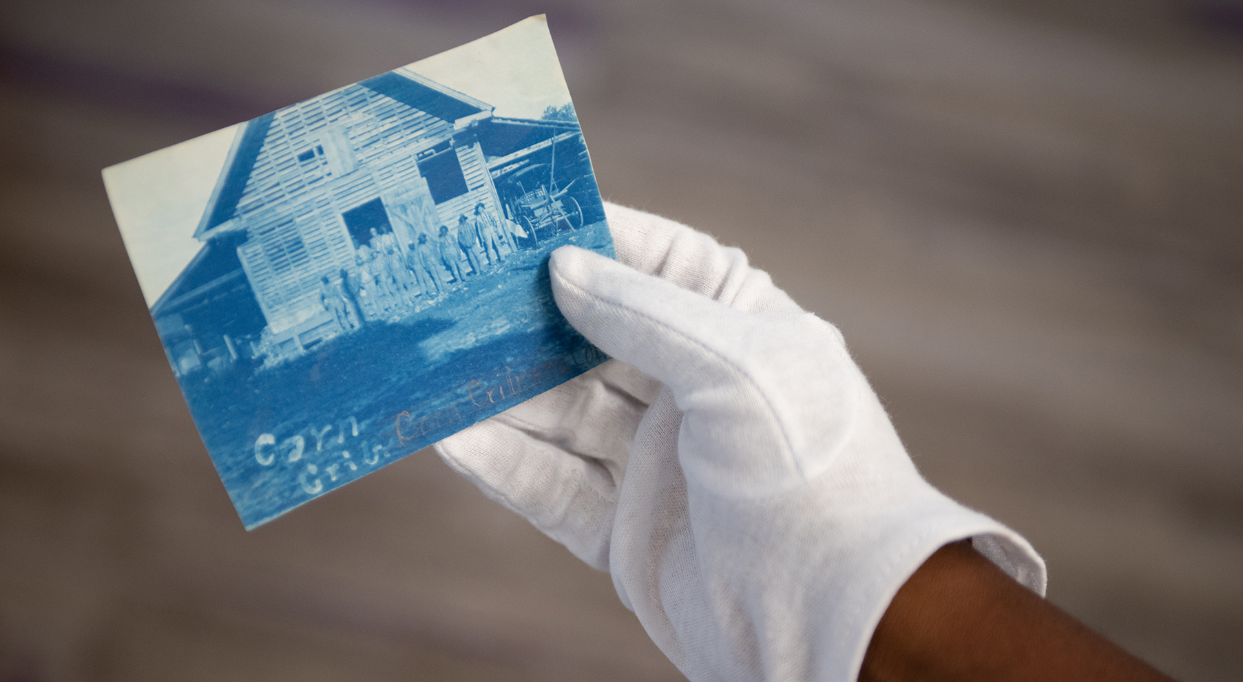 a gloved hand holding a historical picture of people standing in front of a barn