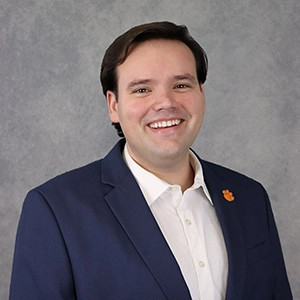 Professional headshot of a smiling young man in a dark blazer and white shirt.