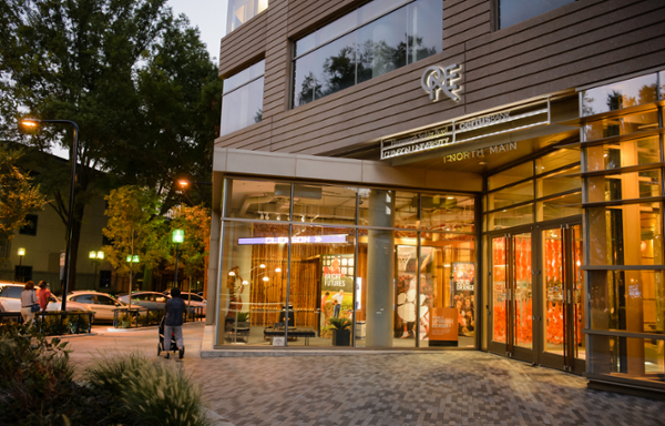 Exterior view of a modern building featuring large glass windows and vibrant signage, set in an urban environment during twilight.