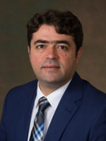 Professional portrait of a man in a navy suit and patterned tie, showcasing a confident expression.