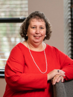 Portrait of a woman in a red sweater with a pearl necklace, smiling and posing in an office setting.