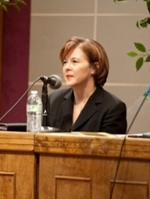 A woman in professional attire speaking into a microphone at a panel discussion.