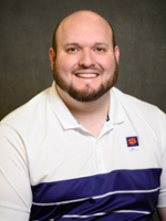 Professional headshot of a smiling man with a beard, wearing a white polo shirt with purple and navy stripes.