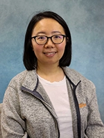 Headshot of a young woman with glasses, wearing a gray sweater, against a soft blue background.