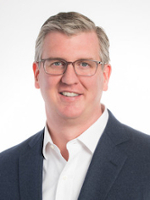 Professional headshot of a man with glasses, wearing a blazer and smiling.