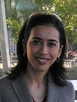 Headshot of a smiling woman with long dark hair, wearing hoop earrings and sunglasses on her head.