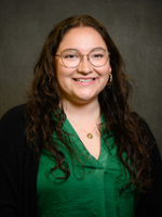A smiling woman with long, wavy hair, wearing glasses and a green blouse.