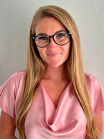 A professional headshot of a woman with long hair, wearing glasses and a pink blouse.