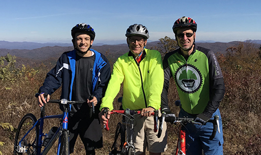 Daniel Cubides, Tom Johnson and David Taylor standing on their bikes on top of Sassafras Mountain.