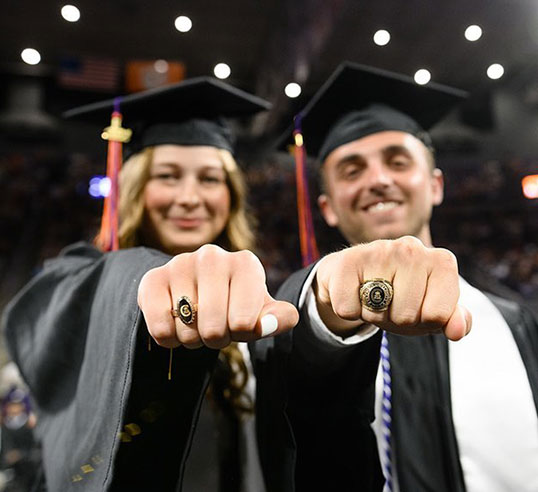 Two students at graduation showing college rings