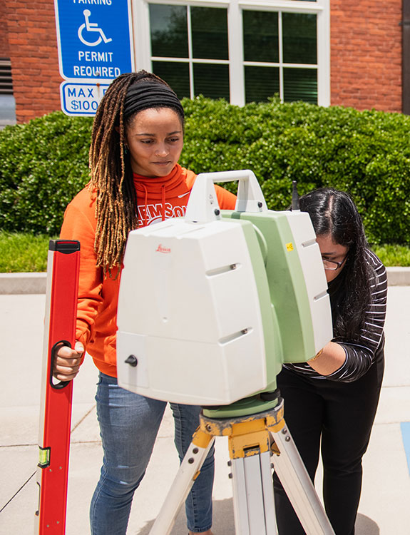 Two females using survey equipment outside of Sikes Hall.