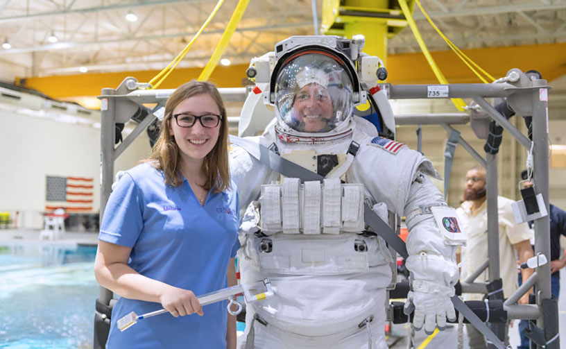 Female student standing with man in space suit at NASA.
