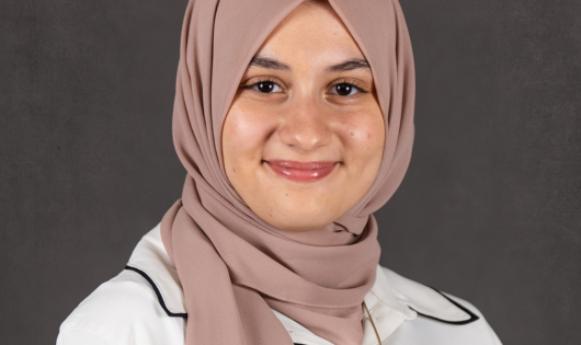 A young woman wearing a hijab smiles at the camera. 