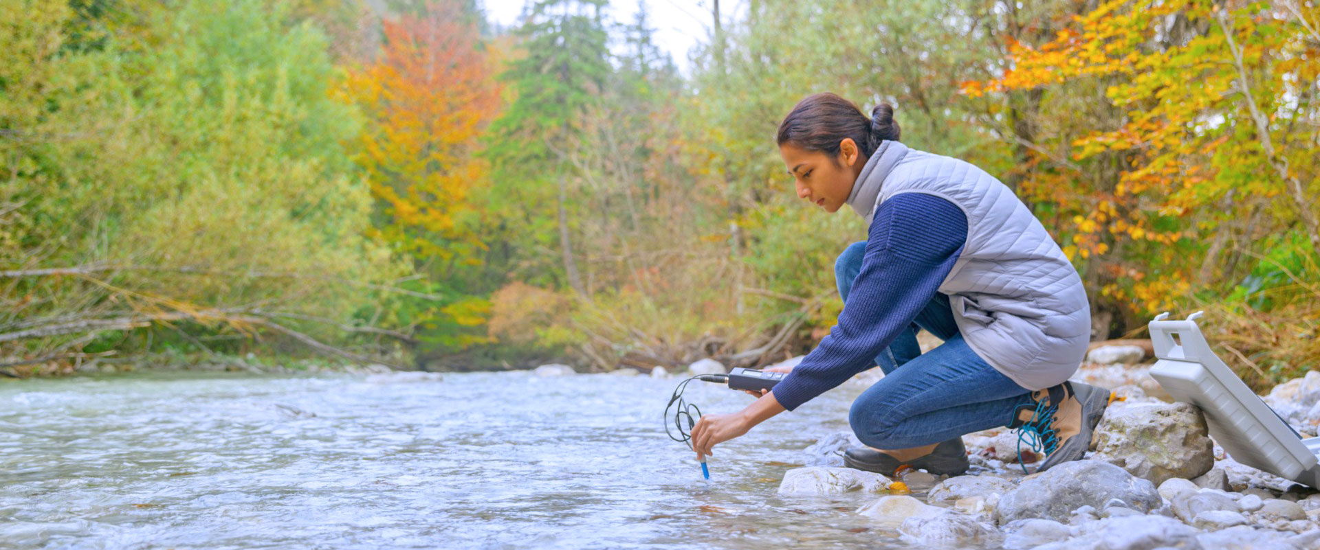 Female taking water measurements along river.