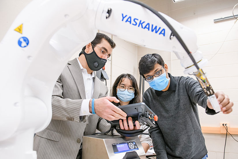 Two male and a female coworkers look at a robotic arm