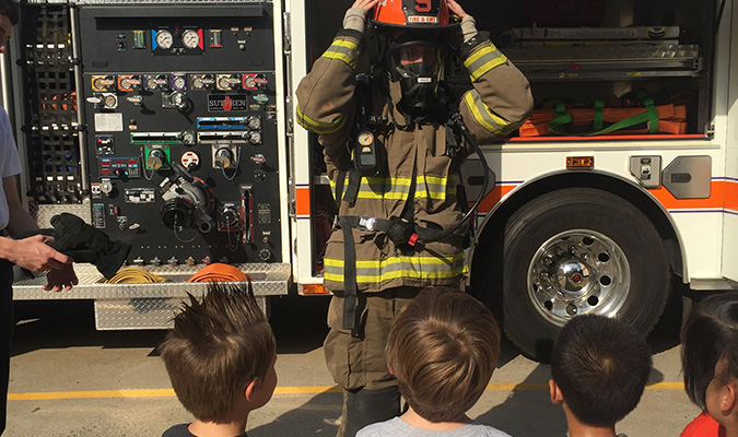 Three young kids look on as a firefighter puts on his gear.