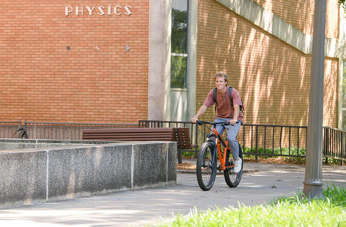 Student riding bicycle in front of Kinard building.