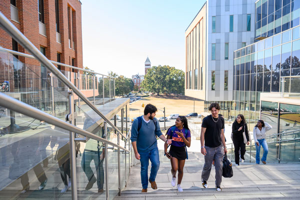 students walk up the steps of the college of business with bowman field and Tillman hall in the background