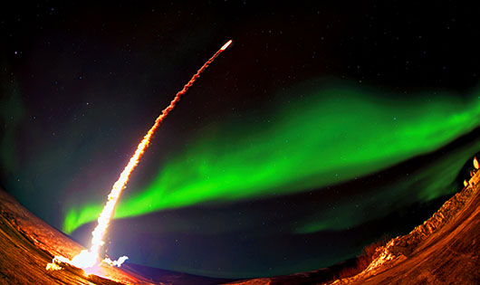 Rocket launching into night sky with green aurora in background.
