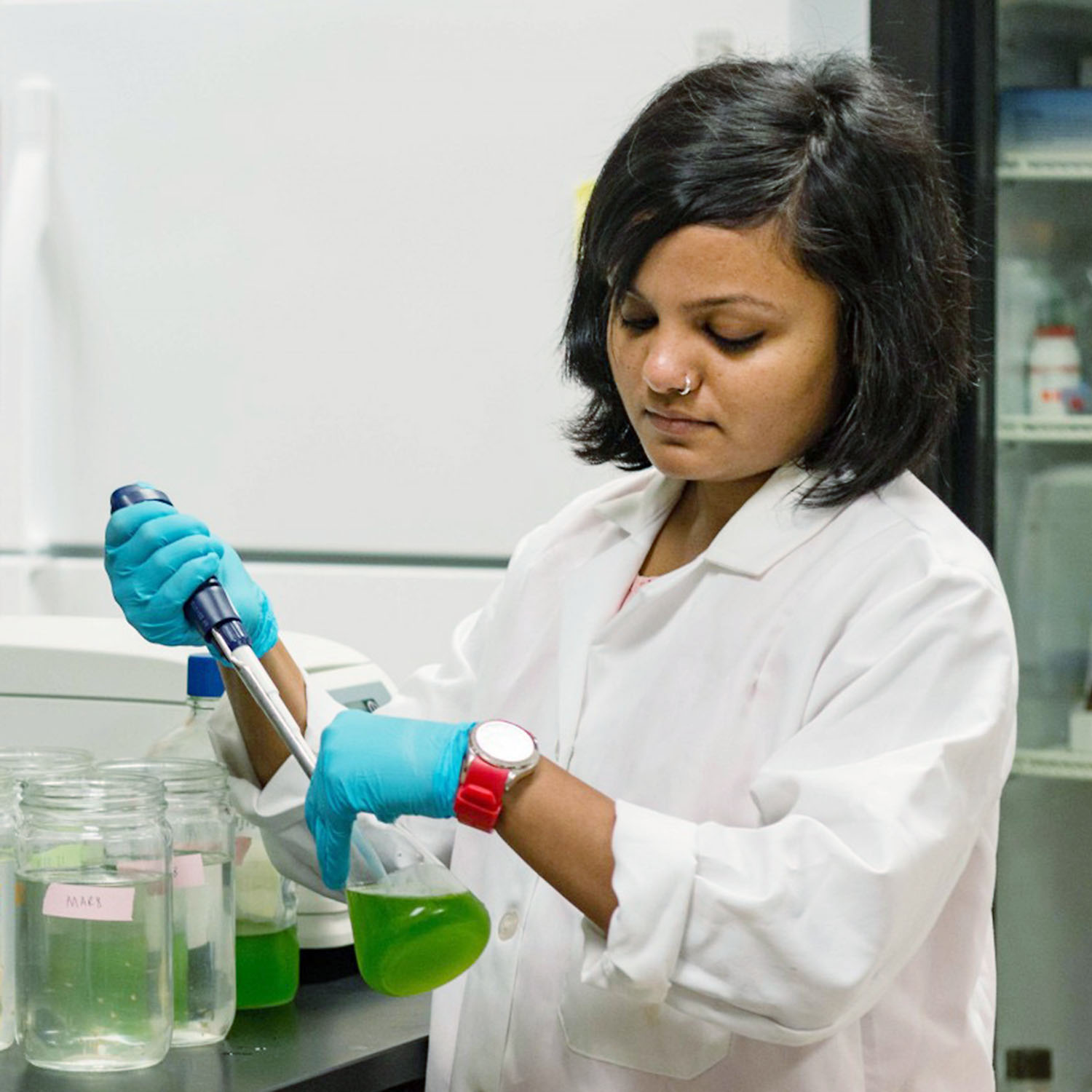 Woman in lab with a pipette and flask with green liquid.