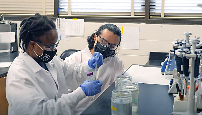 Two female students in lab, wearing masks. Frame from video.