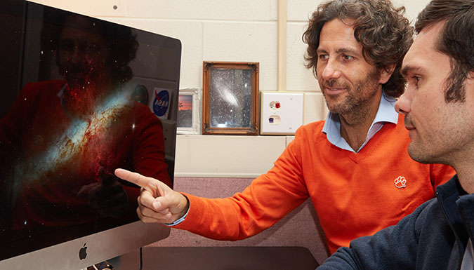 Faculty member and student looking at computer screen with cosmos image.