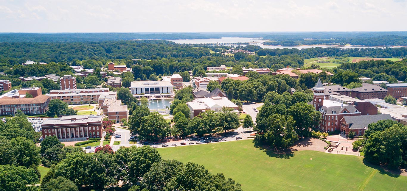 An overheard shot of Clemson University’s main campus shows several landmarks including Bowman Field, Tillman Hall, the Reflection Pond and R.M. Cooper Library among other brick academic buildings and green trees. 