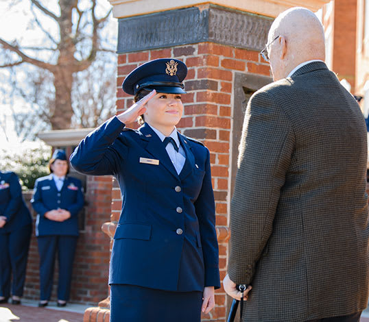 Female air force cadet in uniform smiles and salutes an elderly man.
