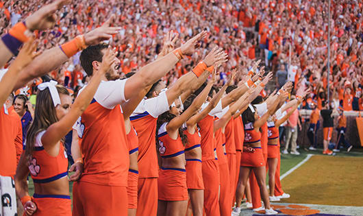 Clemson cheerleaders, surrounded by fans in the east end zone of Memorial Stadium, wave their hands in the alma mater salute.
