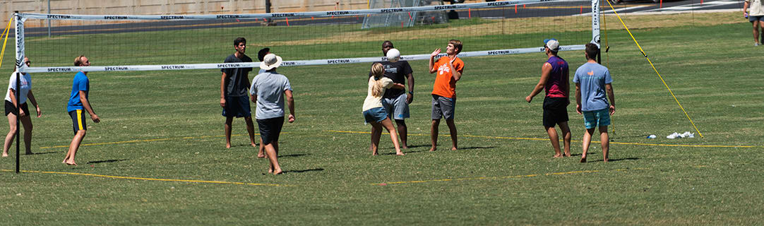 Eight college students play volleyball in the sun on Bowman Field.