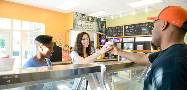 A male student worker in the '55 Exchange serves ice cream to female students in the on-campus ice cream shop.
