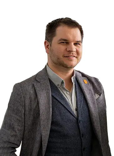 A man wearing a dark gray blazer with an orange Tiger Paw lapel and two gray button-down shirts.